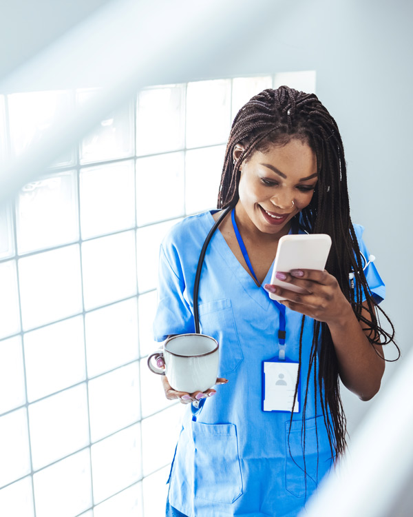 nurse in blue scrubs drinking tea smiling at phone